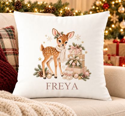 Personalised white Christmas cushion with a fawn in a cream scarf beside a stack of presents and a name printed underneath, on a festive sofa