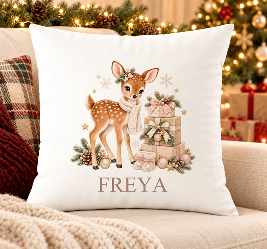 Personalised white Christmas cushion with a fawn in a cream scarf beside a stack of presents and a name printed underneath, on a festive sofa