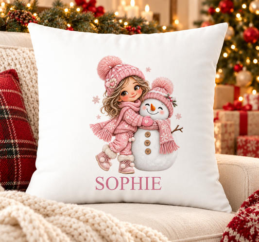 Personalised white Christmas cushion with a girl in pink hat hugging a snowman and a name printed underneath, on a festive sofa