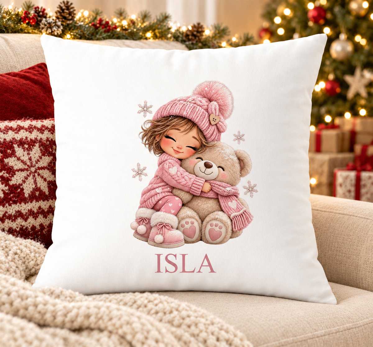 Personalised white Christmas cushion with a girl in pink knits hugging a teddy and a name printed underneath, on a festive sofa