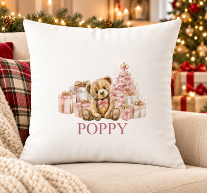 Personalised white Christmas cushion with a teddy bear with pink presents and a pink tree and a name printed underneath, on a festive sofa