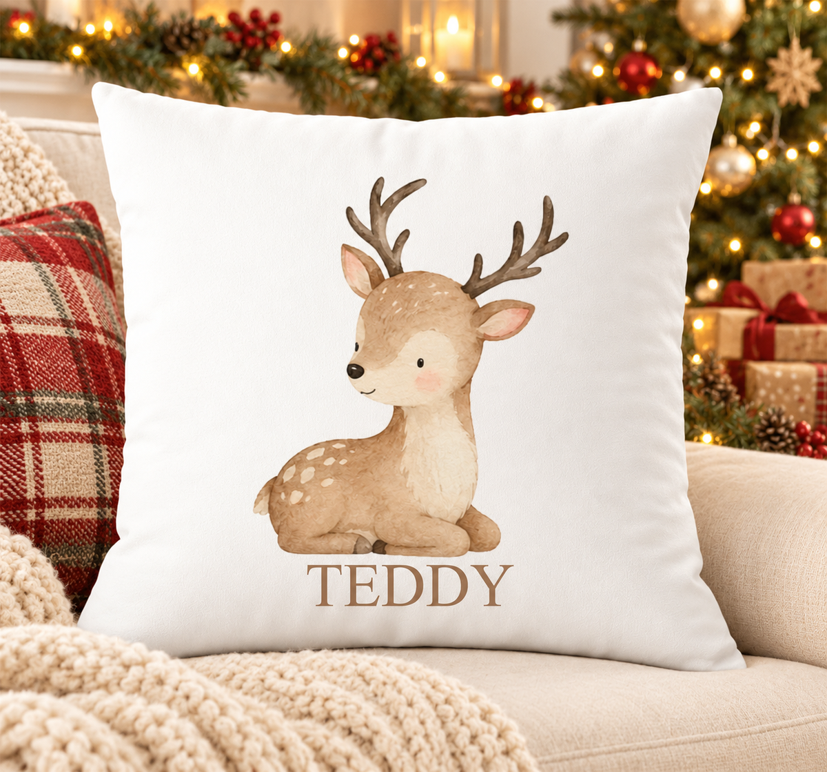 Personalised white Christmas cushion with a simple resting reindeer in soft natural tones and a name printed underneath, on a festive sofa