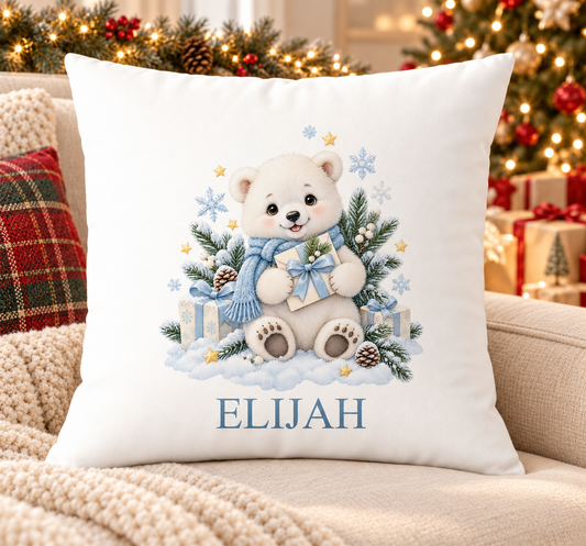 Personalised white Christmas cushion with a polar bear cub in a blue scarf holding a present and a name printed underneath, on a festive sofa