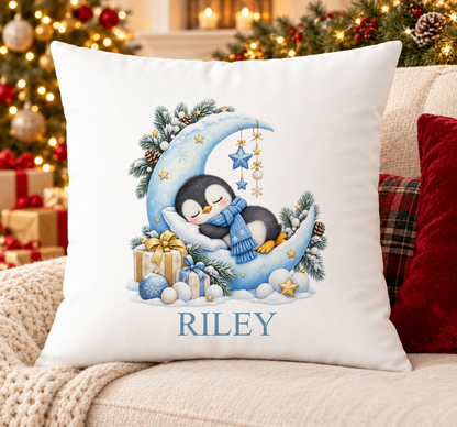 Personalised white Christmas cushion with a sleepy penguin on a crescent moon and a name printed underneath, on a festive sofa