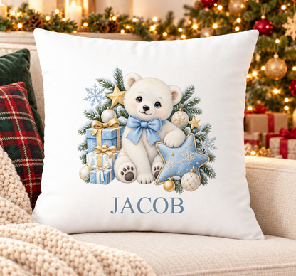 Personalised white Christmas cushion with a polar bear with a blue bow, presents and a star and a name printed underneath, on a festive sofa