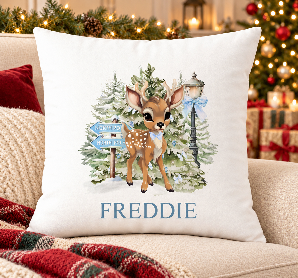 Personalised white Christmas cushion with a fawn beside a blue North Pole signpost in a snowy forest and a name printed underneath, on a festive sofa