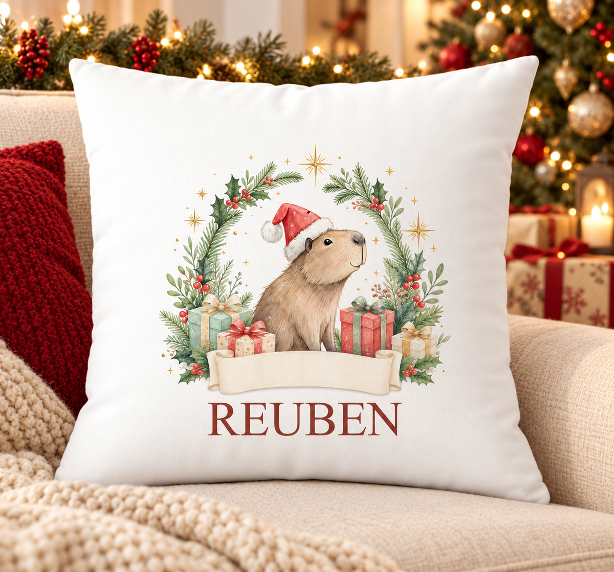 Personalised white Christmas cushion with a capybara in a Santa hat inside a festive wreath and a name printed underneath, on a festive sofa