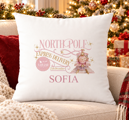 Personalised white Christmas cushion with a pink 'North Pole Express Delivery' design with a steam train and a name printed underneath, on a festive sofa