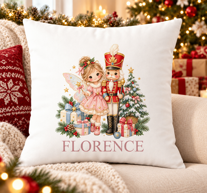 Personalised white Christmas cushion with a pink fairy with a nutcracker soldier beside a Christmas tree and a name printed underneath, on a festive sofa