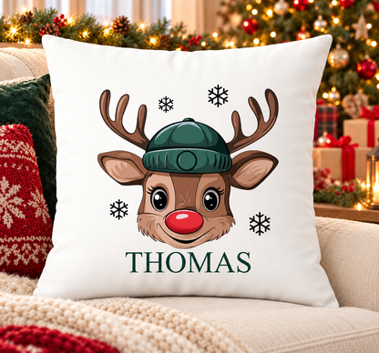 Personalised white Christmas cushion with a cheeky reindeer face in a green beanie and a name printed underneath, on a festive sofa