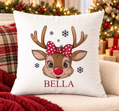 Personalised white Christmas cushion with a reindeer face with a red polka dot bow and a name printed underneath, on a festive sofa