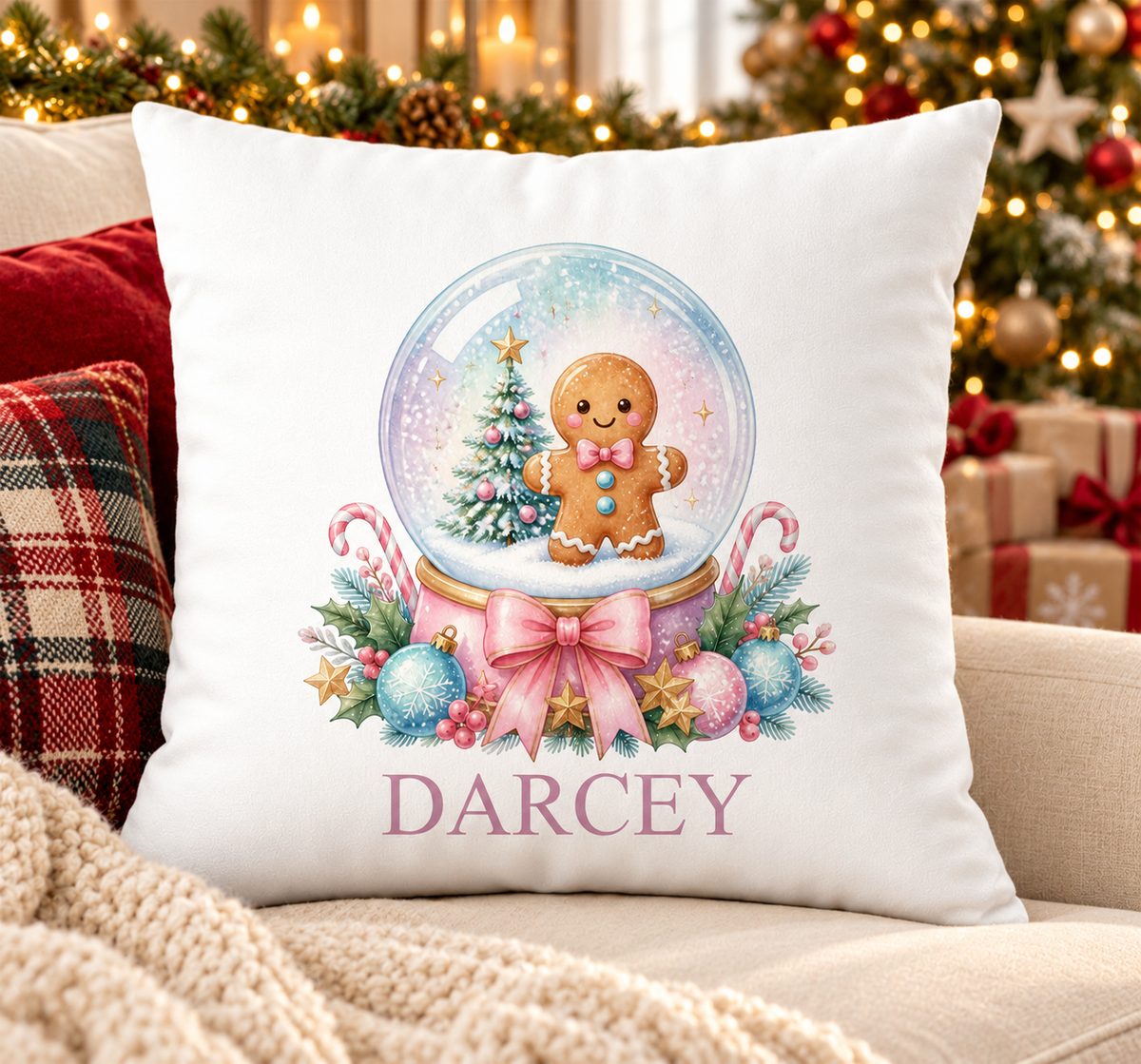 Personalised white Christmas cushion with a gingerbread man inside a snow globe with pastel baubles and a name printed underneath, on a festive sofa