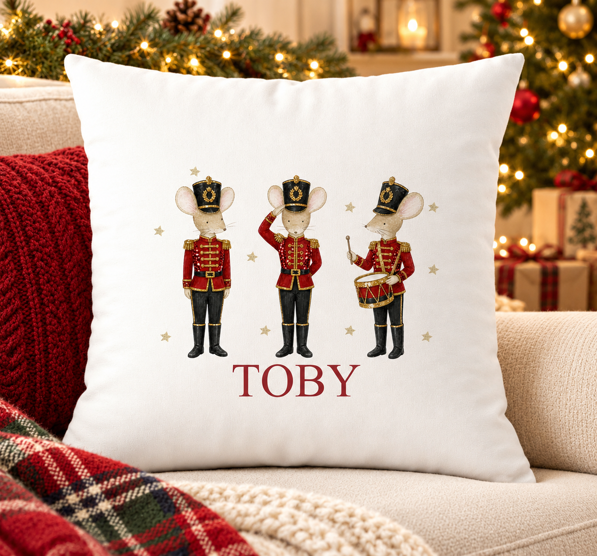 Personalised white Christmas cushion with three mice dressed as nutcracker soldiers and a name printed underneath, on a festive sofa