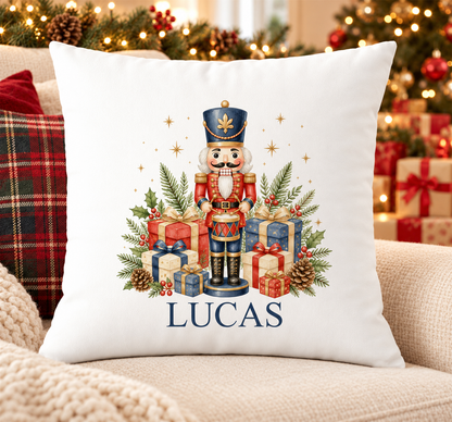 Personalised white Christmas cushion with a nutcracker soldier playing a drum among presents and a name printed underneath, on a festive sofa