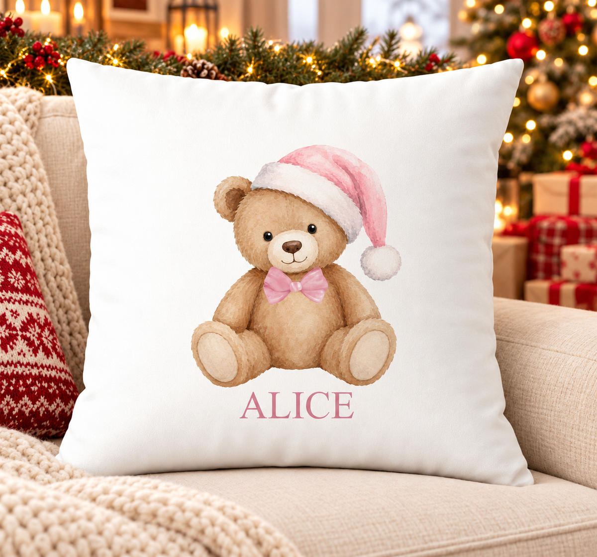 Personalised white Christmas cushion with a teddy bear in a pink Santa hat and bow and a name printed underneath, on a festive sofa