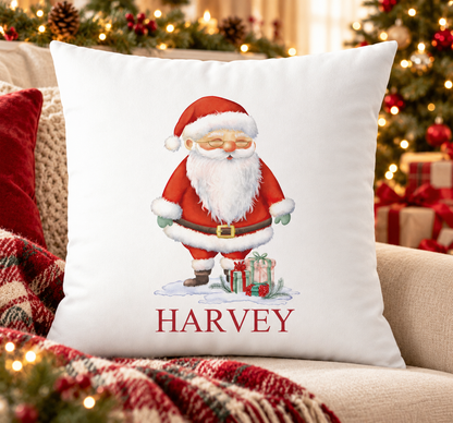 Personalised white Christmas cushion with a jolly Santa standing with presents and a name printed underneath, on a festive sofa