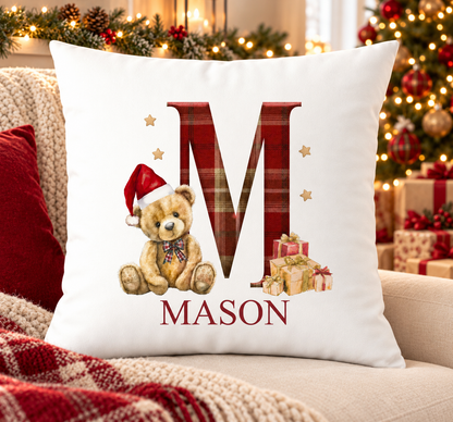 Personalised white Christmas cushion with a large red tartan initial with a teddy in a Santa hat and a name printed underneath, on a festive sofa