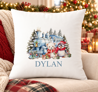 Personalised white Christmas cushion with a blue Christmas train with a polar bear and penguin and a name printed underneath, on a festive sofa