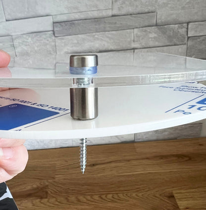 Close-up of the acrylic door plaque's stainless steel mount, showing the clear front plate, white back plate and fixing screw.