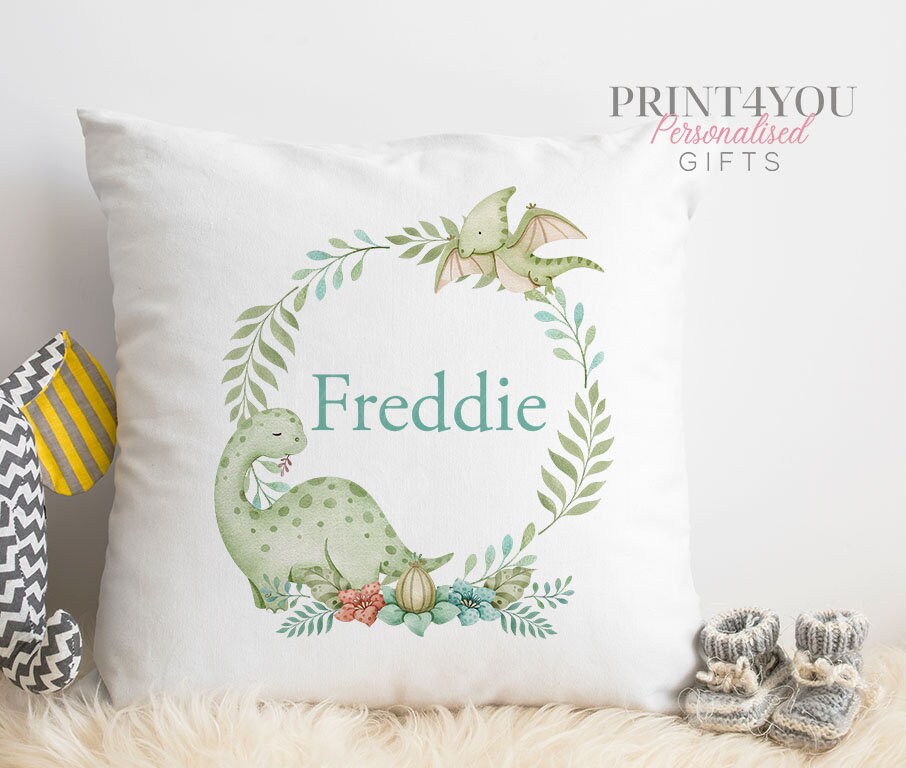 White square cushion with a green dinosaur wreath design and the personalised name Freddie printed in teal lettering.