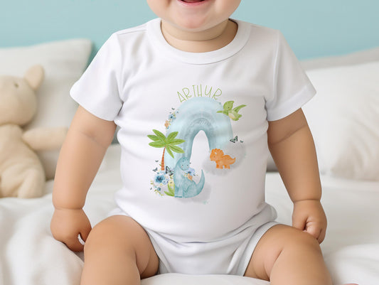 White cotton baby bib printed with dinosaurs on a rainbow design and baby's name.