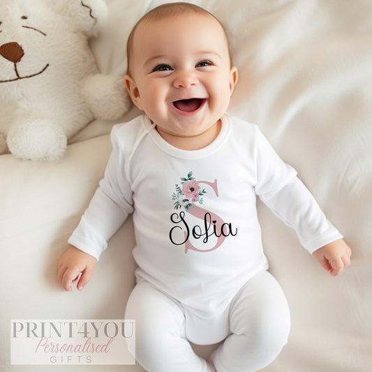 Personalised newborn sleepsuit in soft white cotton with a delicate pink floral print and baby girl's name across the chest.